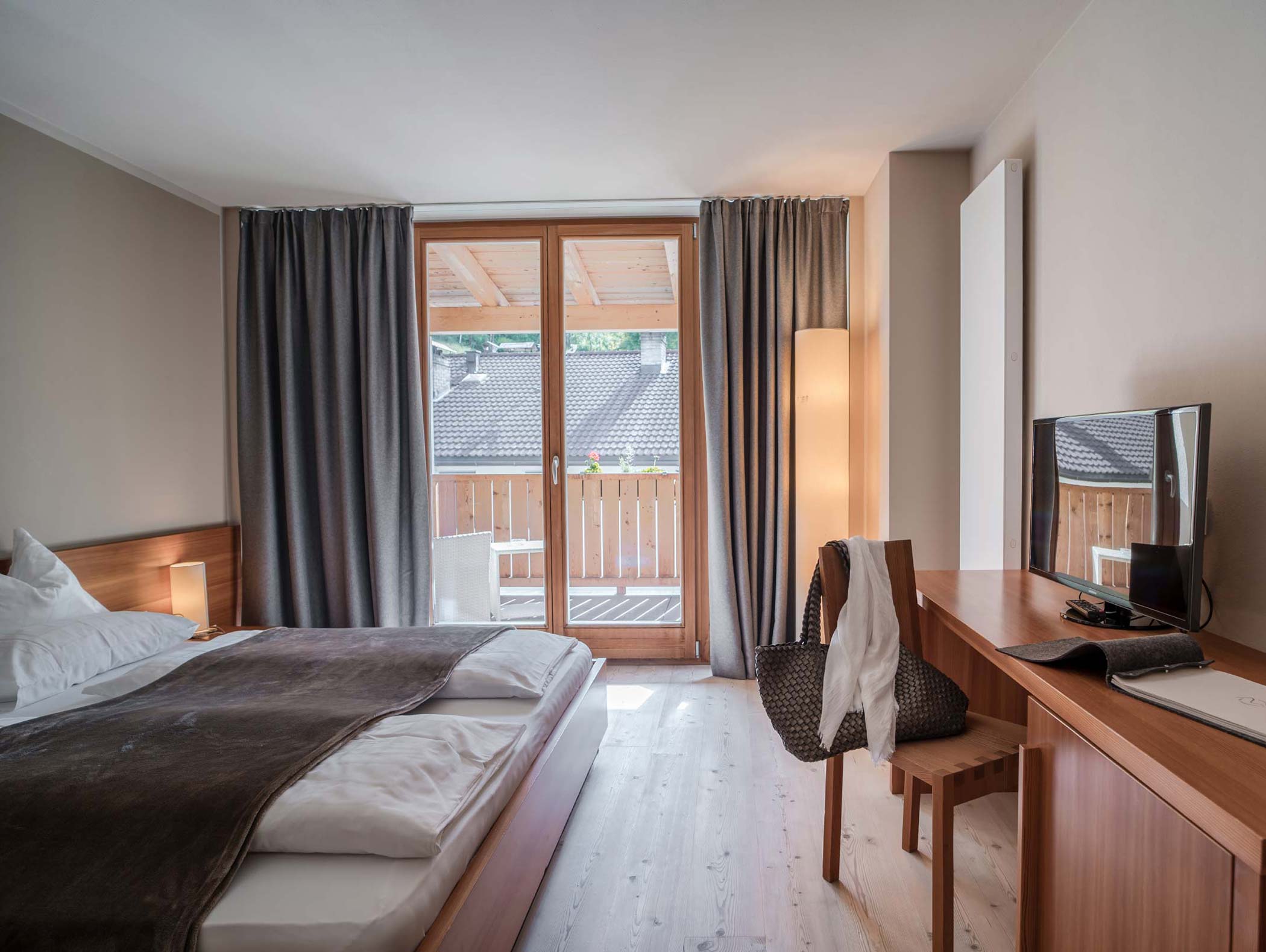 Modernes Hotelzimmer mit Doppelbett, Schreibtisch, TV und Balkon mit Holzgeländer und Sitzgelegenheit im Freien. - Hotel Moosmair