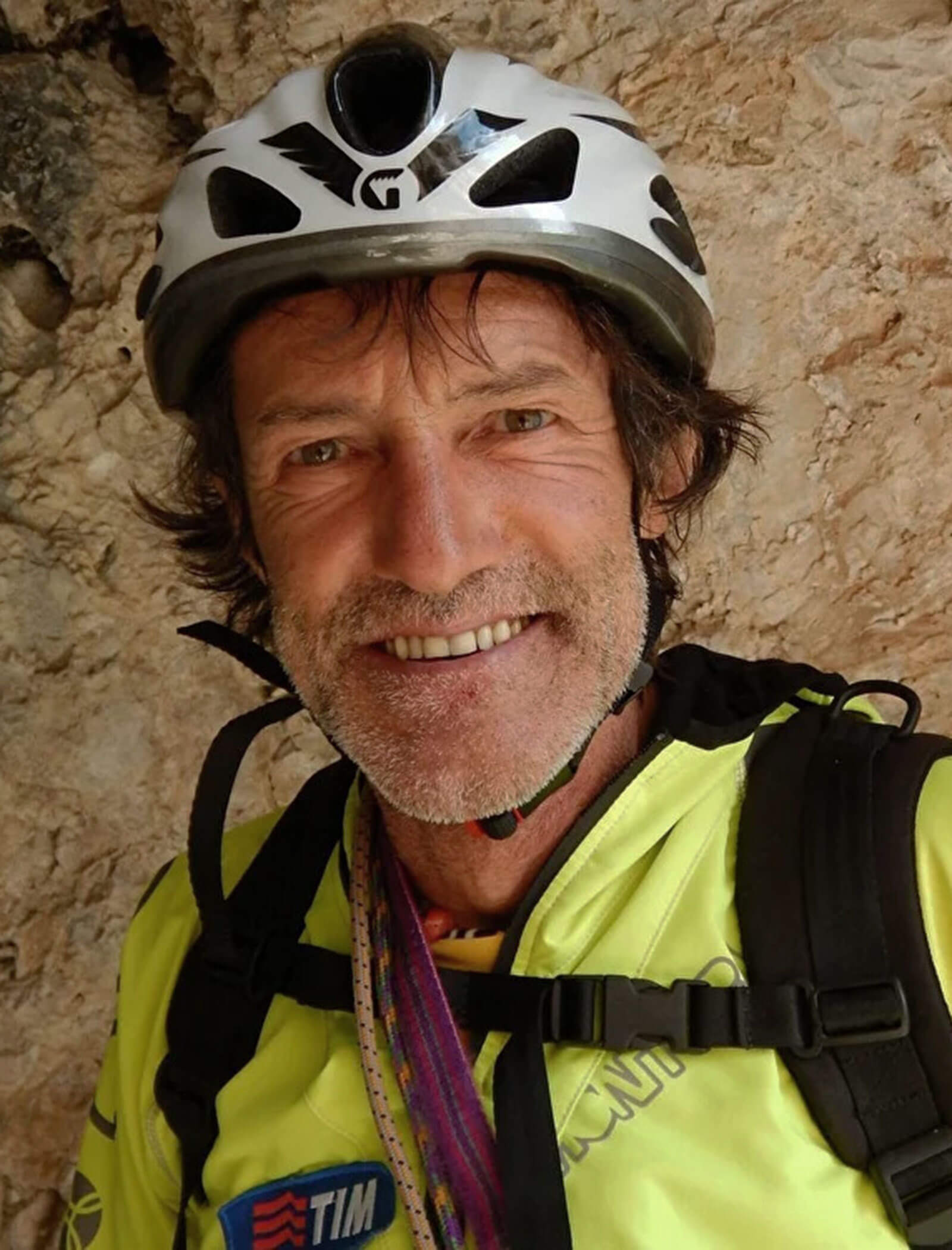 Ein Mann mit Fahrradhelm und Rucksack lächelt vor einem felsigen Hintergrund. - Hotel Moosmair