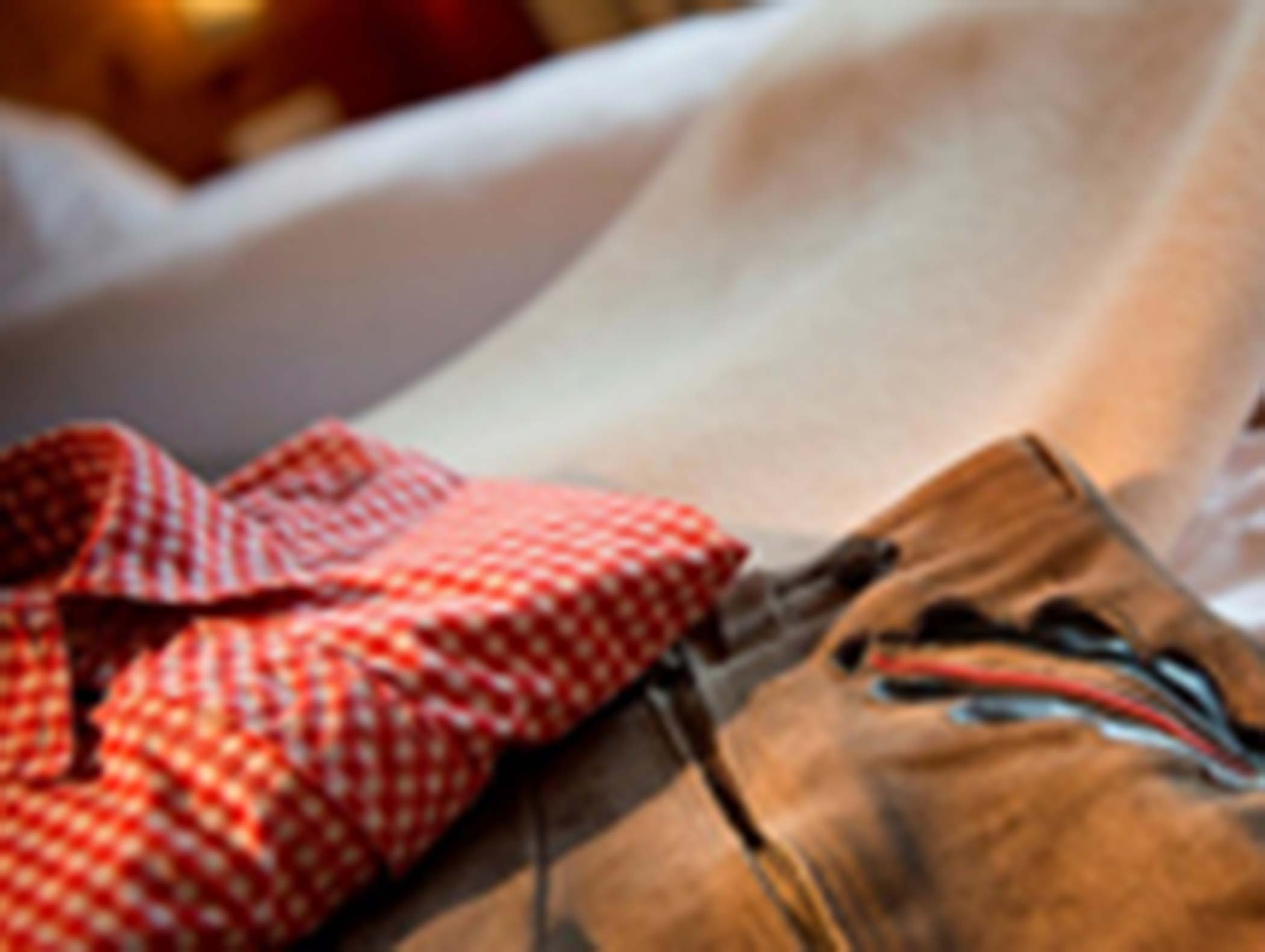Ein rot-weiß-kariertes Hemd und eine braune Hose liegen auf einer hellen Fläche, das Bild ist unscharf. - Hotel Moosmair