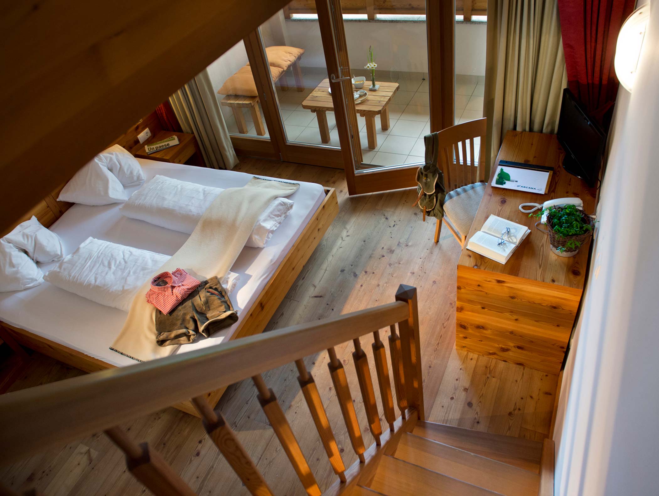 Gemütliches Hotelzimmer mit Doppelbett, Holzmöbeln, Balkon und einem Schreibtisch mit Büchern und einer Pflanze. - Hotel Moosmair