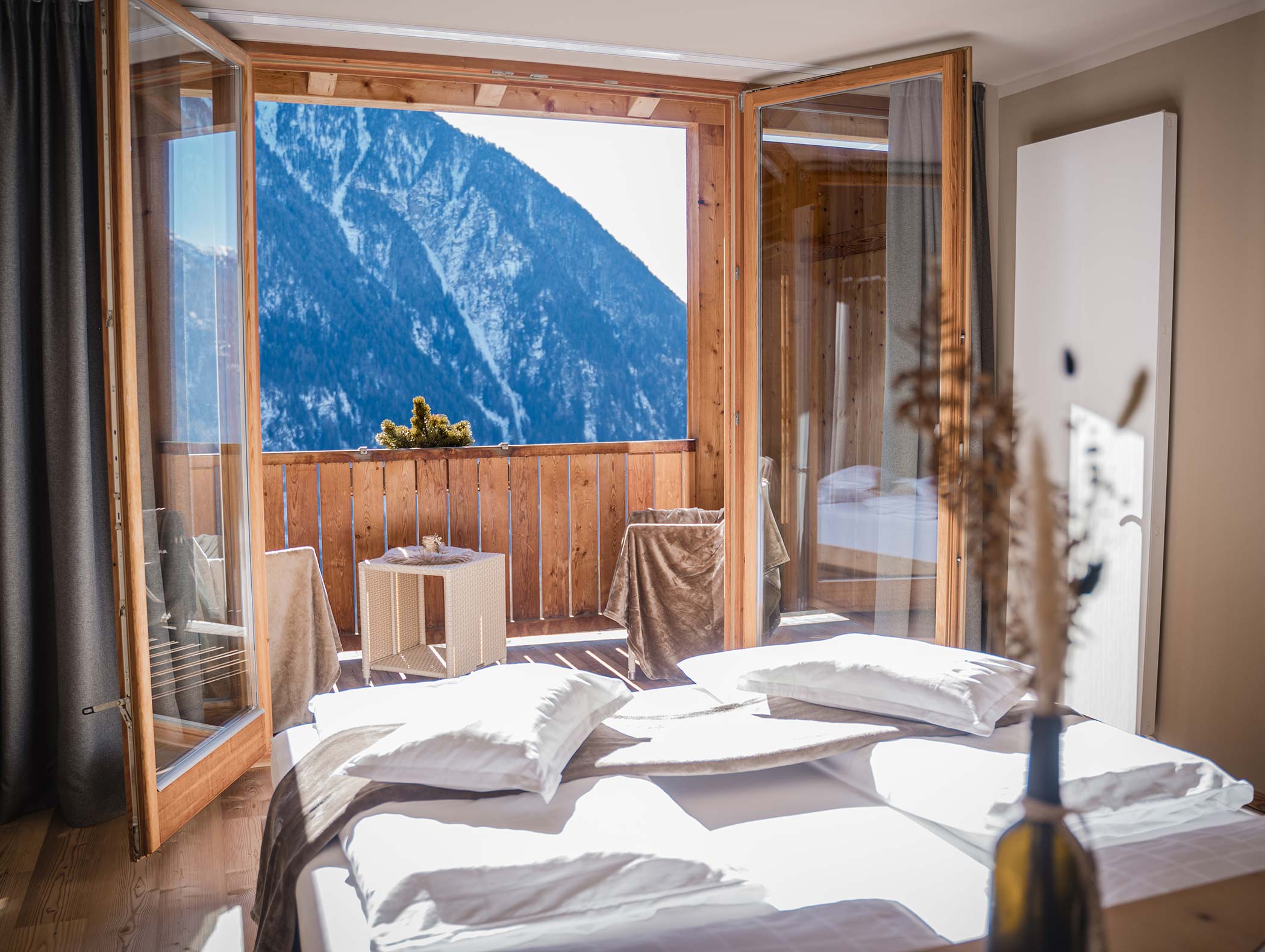 Ein gemütliches Schlafzimmer mit offenen Türen zu einem Balkon, der an einem sonnigen Tag den Blick auf die schneebedeckten Berge freigibt. - Hotel Moosmair