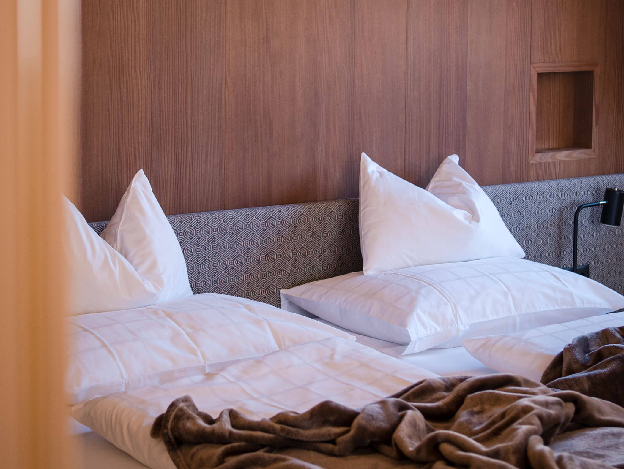 Zwei sauber gemachte Einzelbetten mit weißen Kissen und Bettdecken, brauner Decke und einem Kopfteil aus Holz. - Hotel Moosmair
