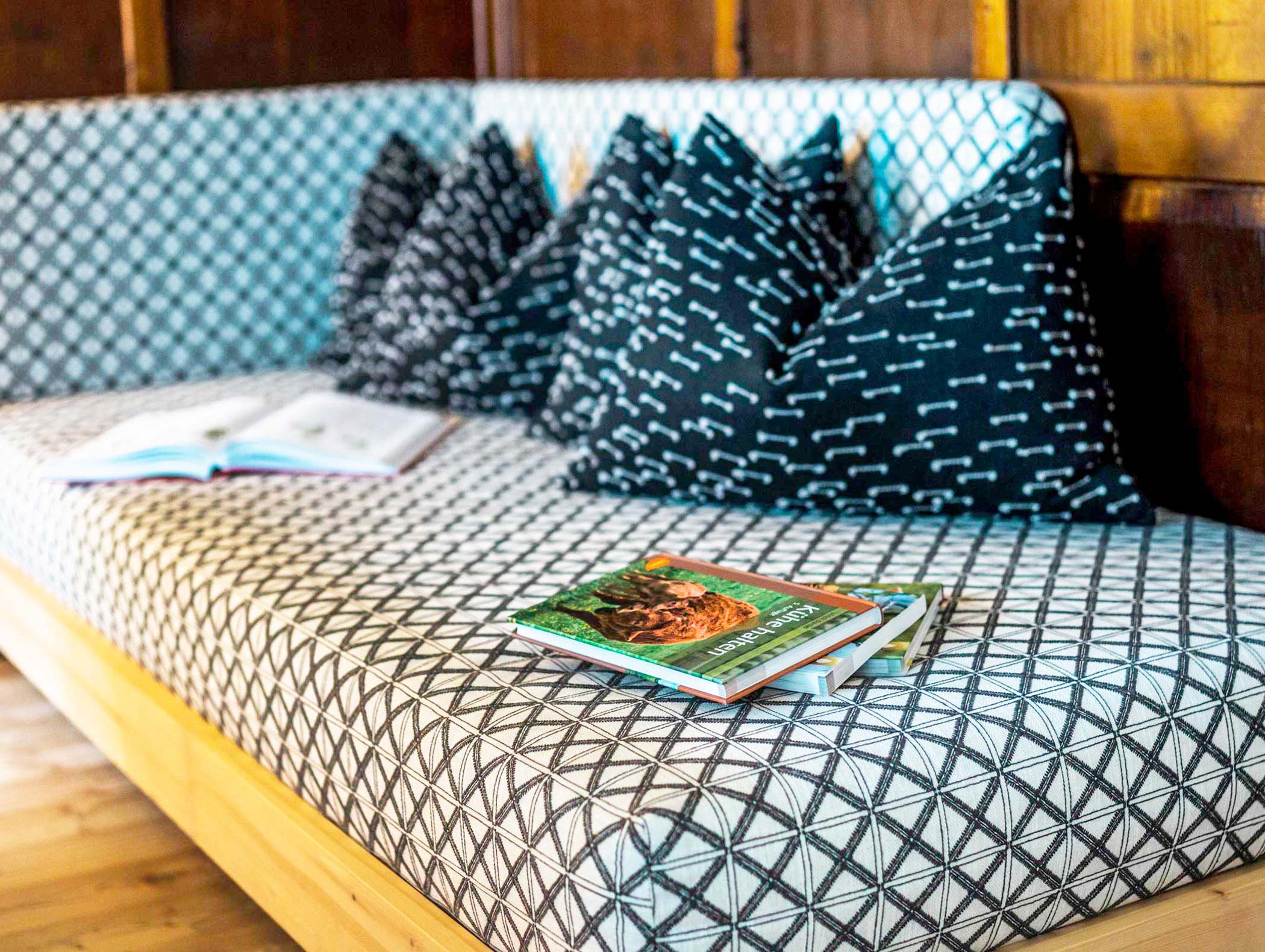 Ein gemustertes Sofa mit schwarz-weißen Kissen und Büchern auf der Sitzfläche. - Hotel Moosmair