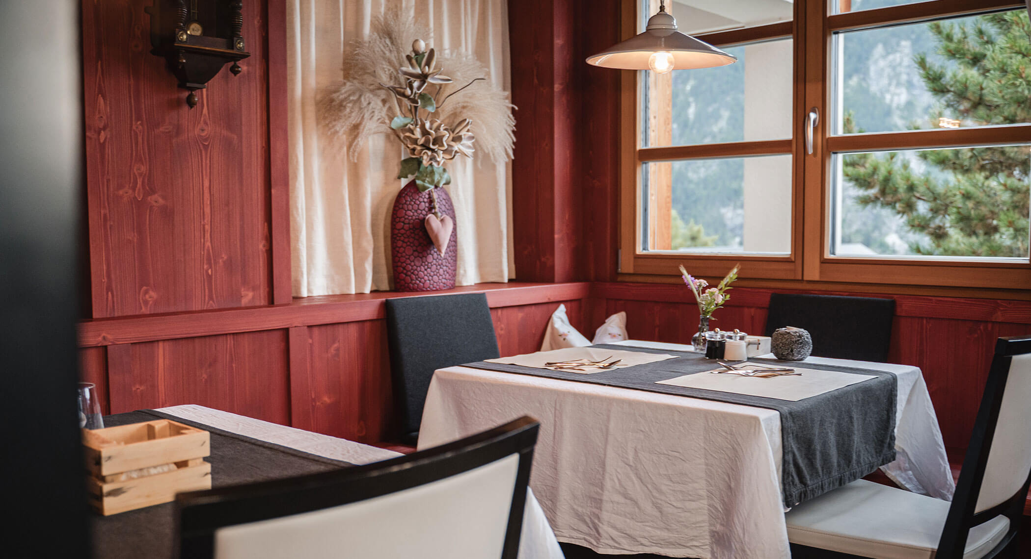 Gemütliche Restaurantecke mit roten Holzwänden, gedeckten Tischen, Blumenvase und großen Fenstern. - Hotel Moosmair