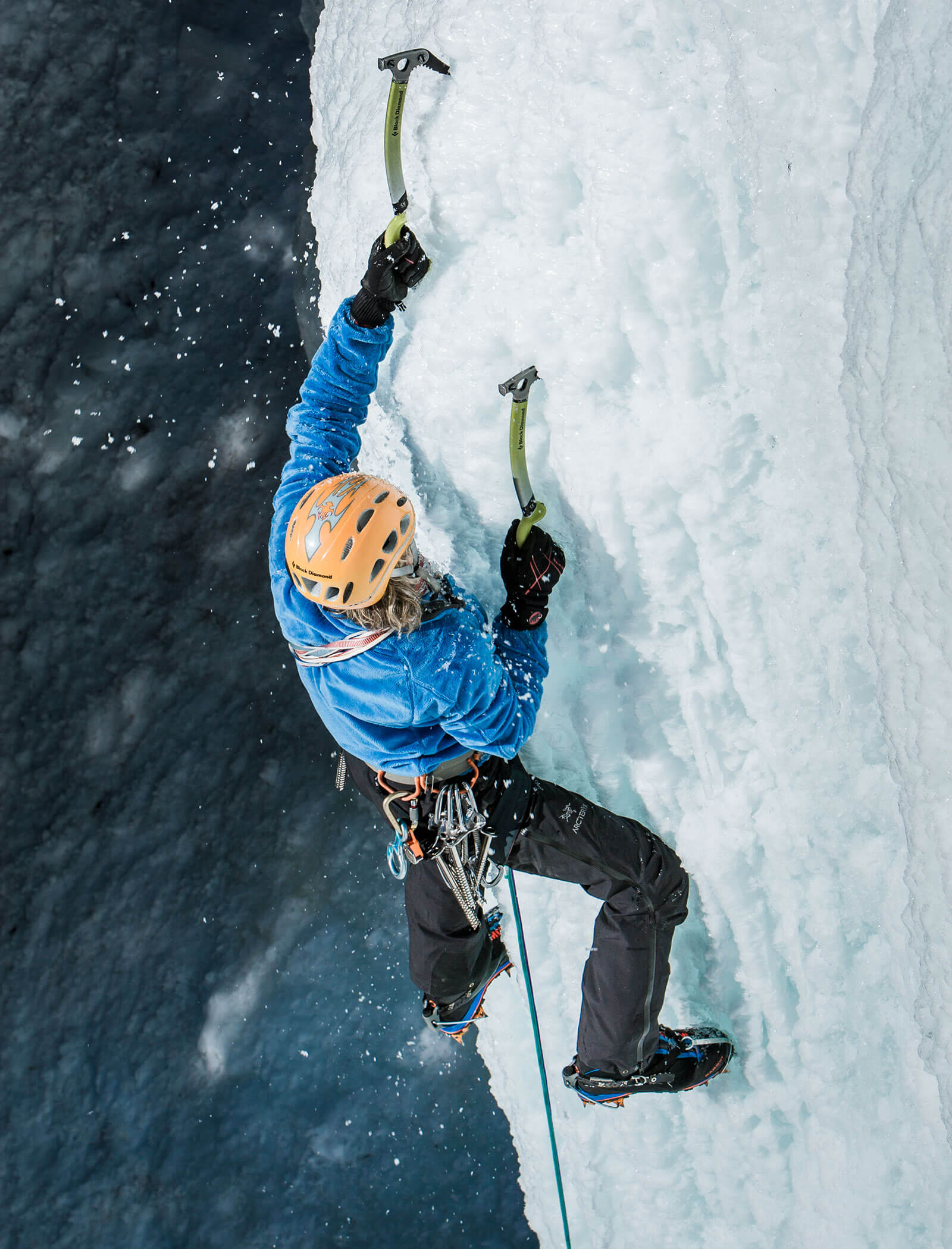 Ein Kletterer mit Helm und blauer Jacke klettert mit Eispickel und Steigeisen eine senkrechte Eiswand hinauf. - Hotel Moosmair