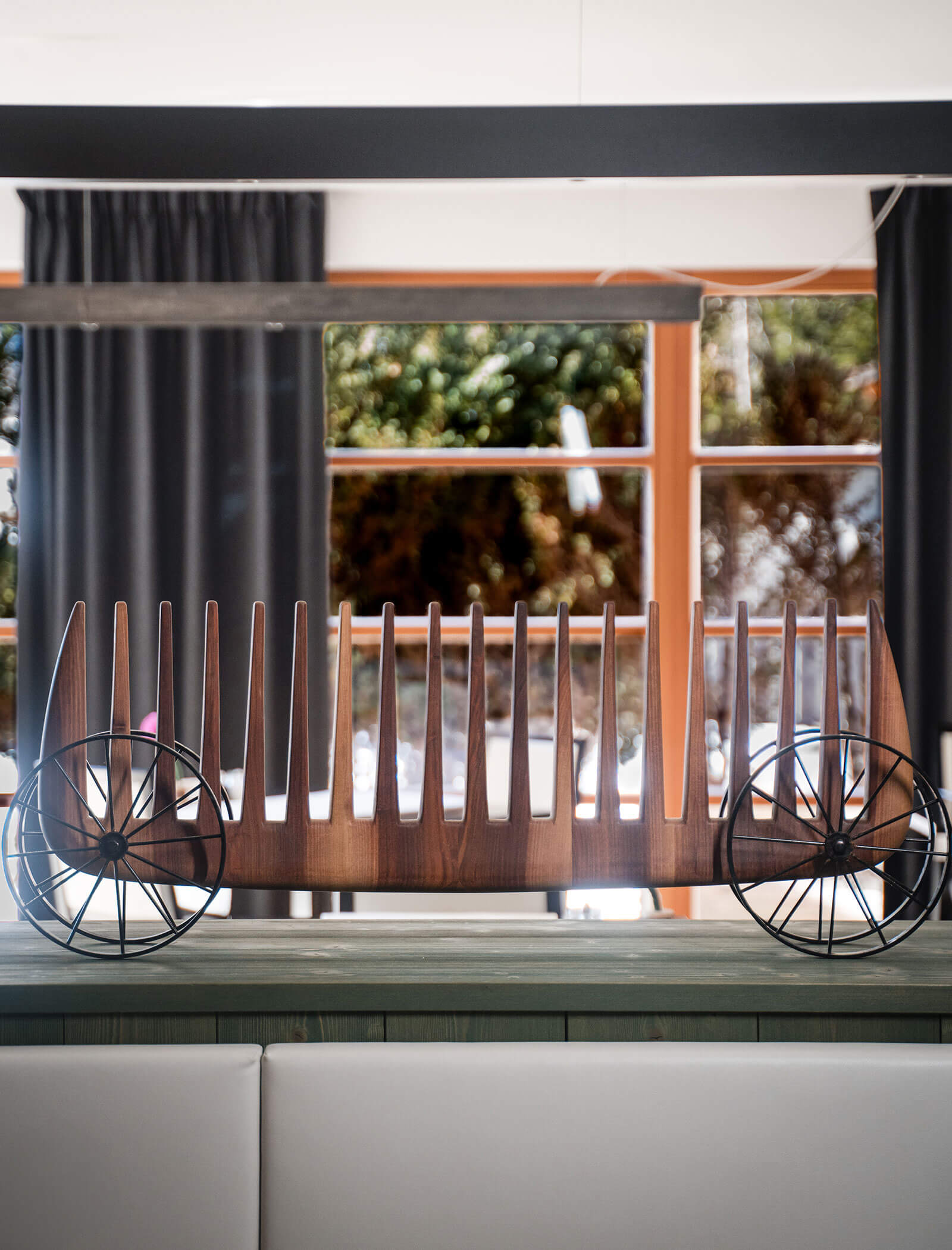 Eine moderne Holzskulptur mit Metallrädern, die an einen minimalistischen, länglichen Wagen auf einem Tisch erinnert. - Hotel Moosmair