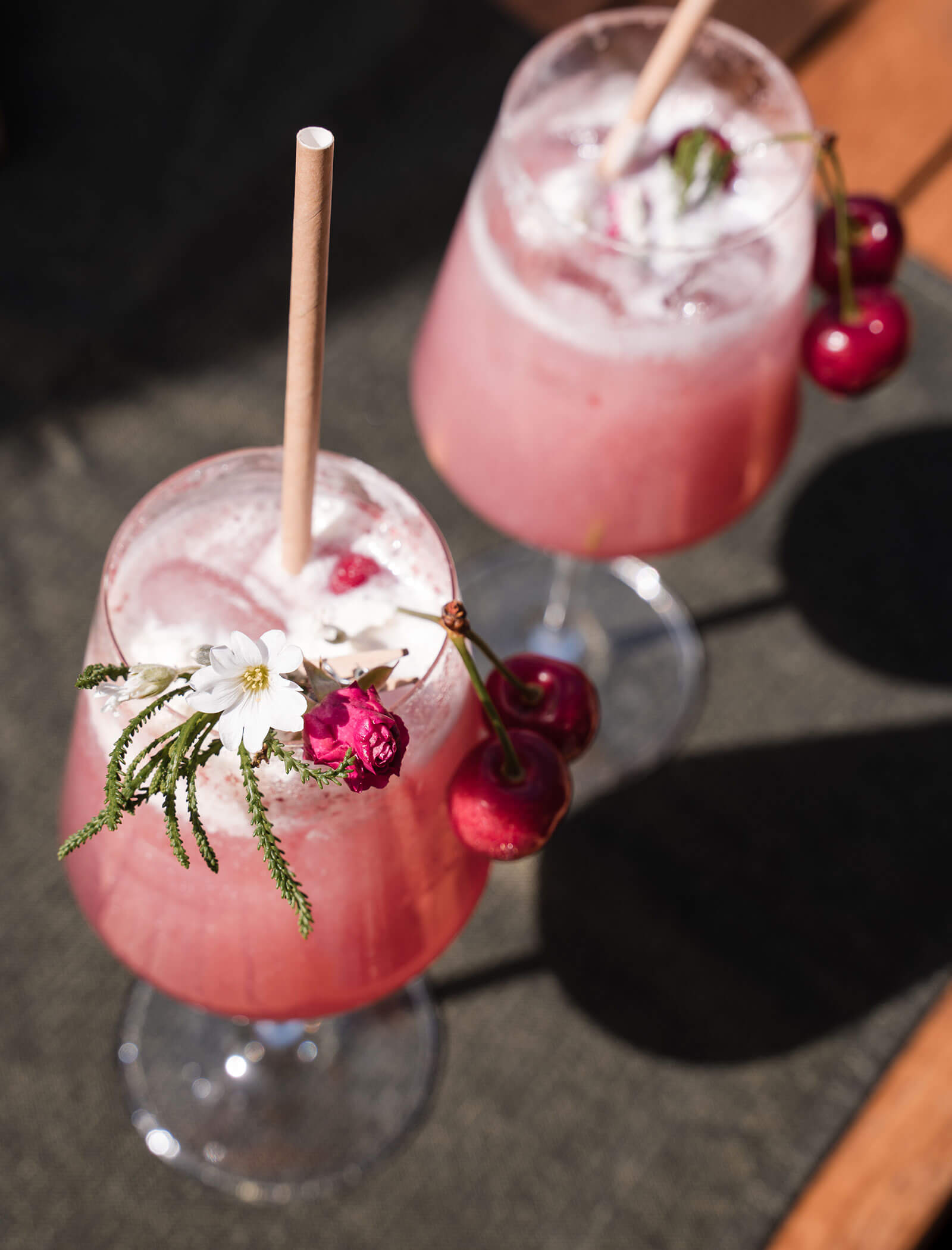 Zwei rosa Cocktails mit Eis, Kirschen und Blumen, serviert in Stielgläsern mit Papierstrohhalmen. - Hotel Moosmair
