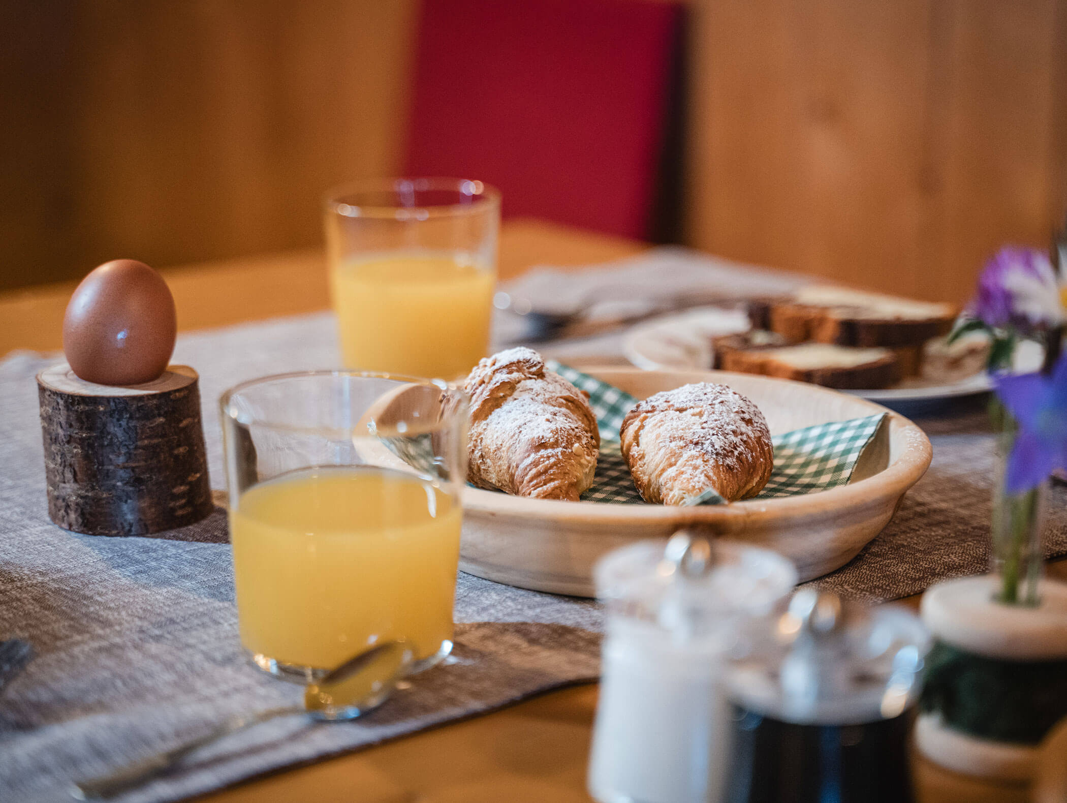 Ein Glas Orangensaft, ein gekochtes Ei, Gebäck mit Puderzucker und Brot auf einem Frühstückstisch. - Hotel Moosmair