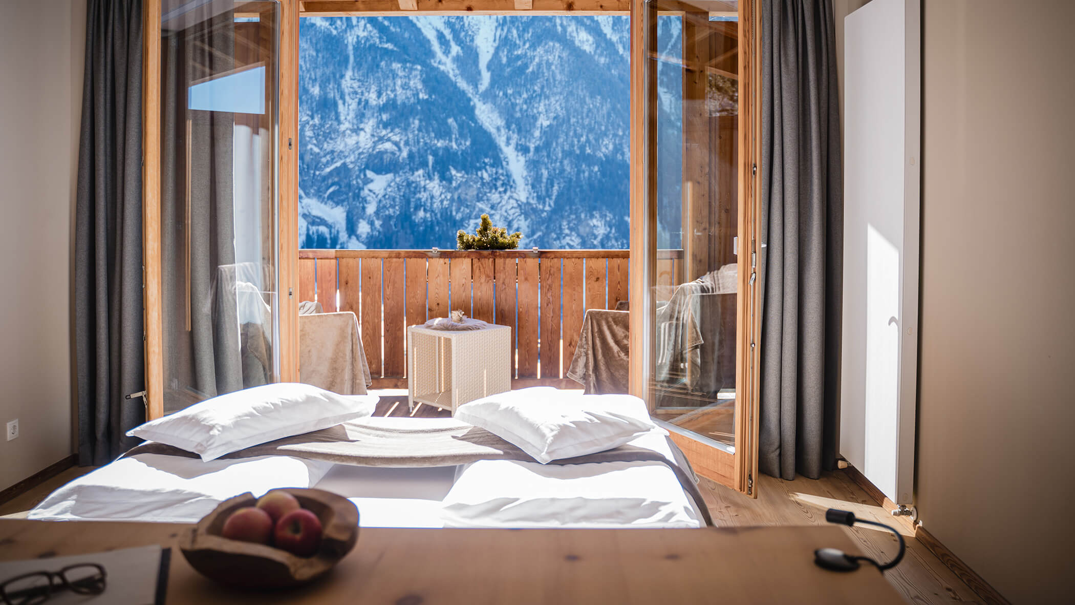 Ein gemütliches Schlafzimmer mit großen Fenstern führt auf einen Balkon mit Blick auf die verschneiten Berge. - Hotel Moosmair