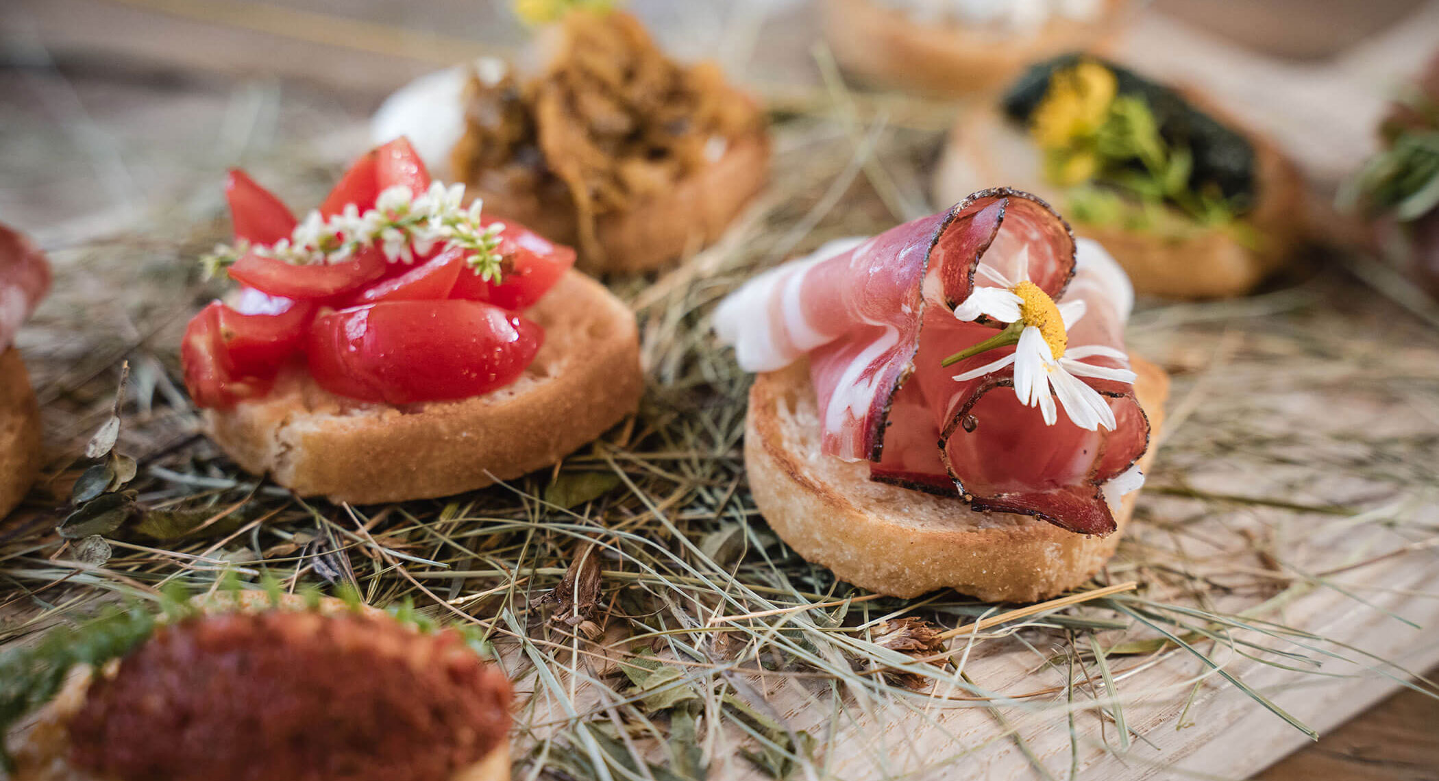 Gemischte Gourmet-Häppchen auf Brot, belegt mit gepökeltem Fleisch, Kirschtomaten, Kräutern und essbaren Blüten. - Hotel Moosmair