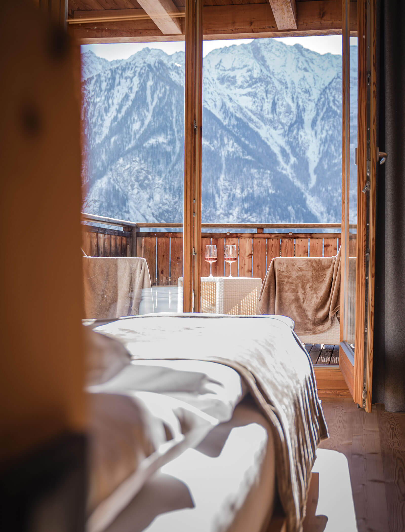 Gemütliches Bett mit Blick auf einen Balkon mit zwei Stühlen, einem Tisch und Bergblick im Hintergrund. - Hotel Moosmair