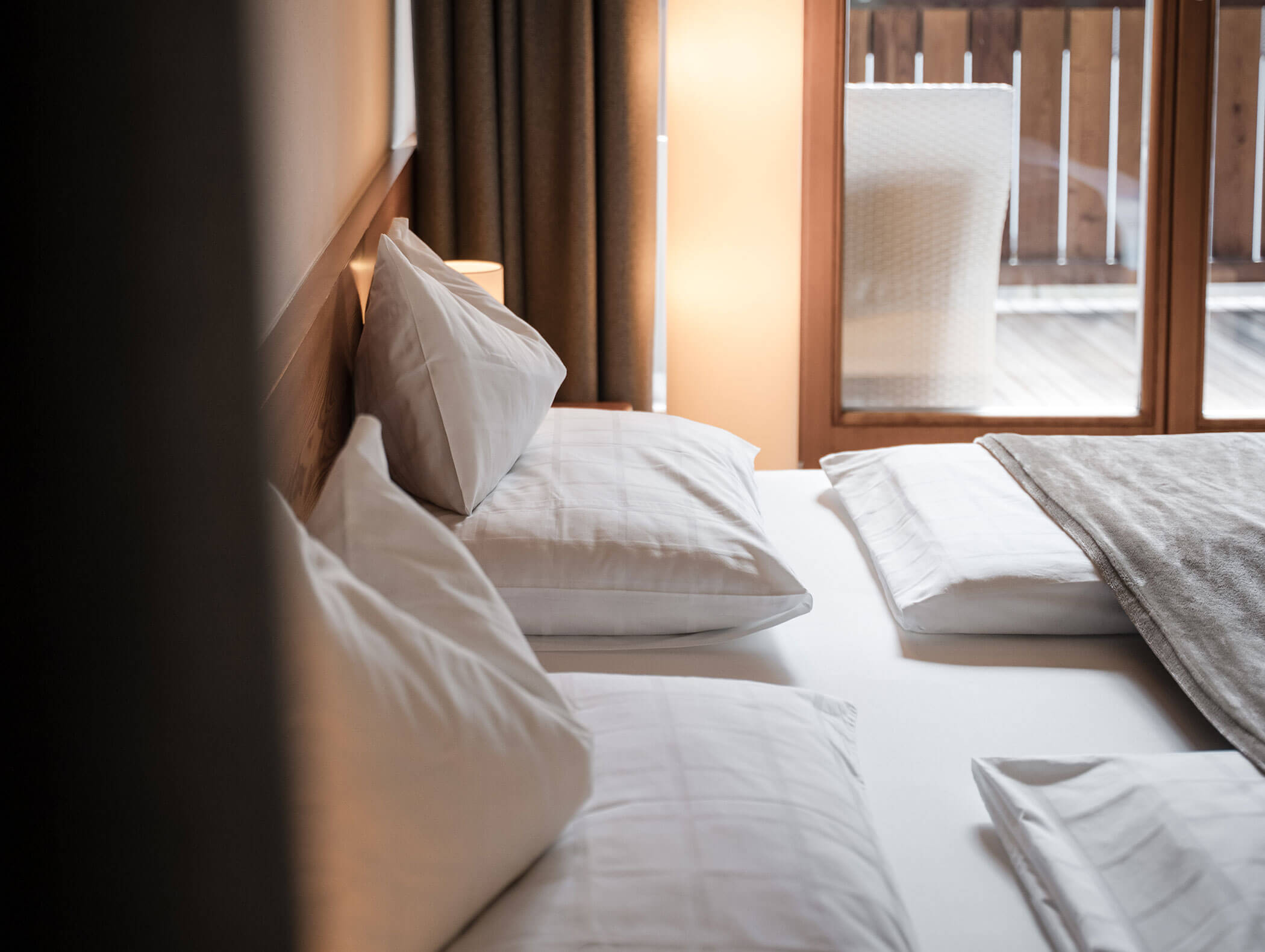 Ein ordentlich gemachtes Bett mit weißen Kissen und Bettzeug, neben einem Fenster und einem Balkon mit natürlichem Licht. - Hotel Moosmair