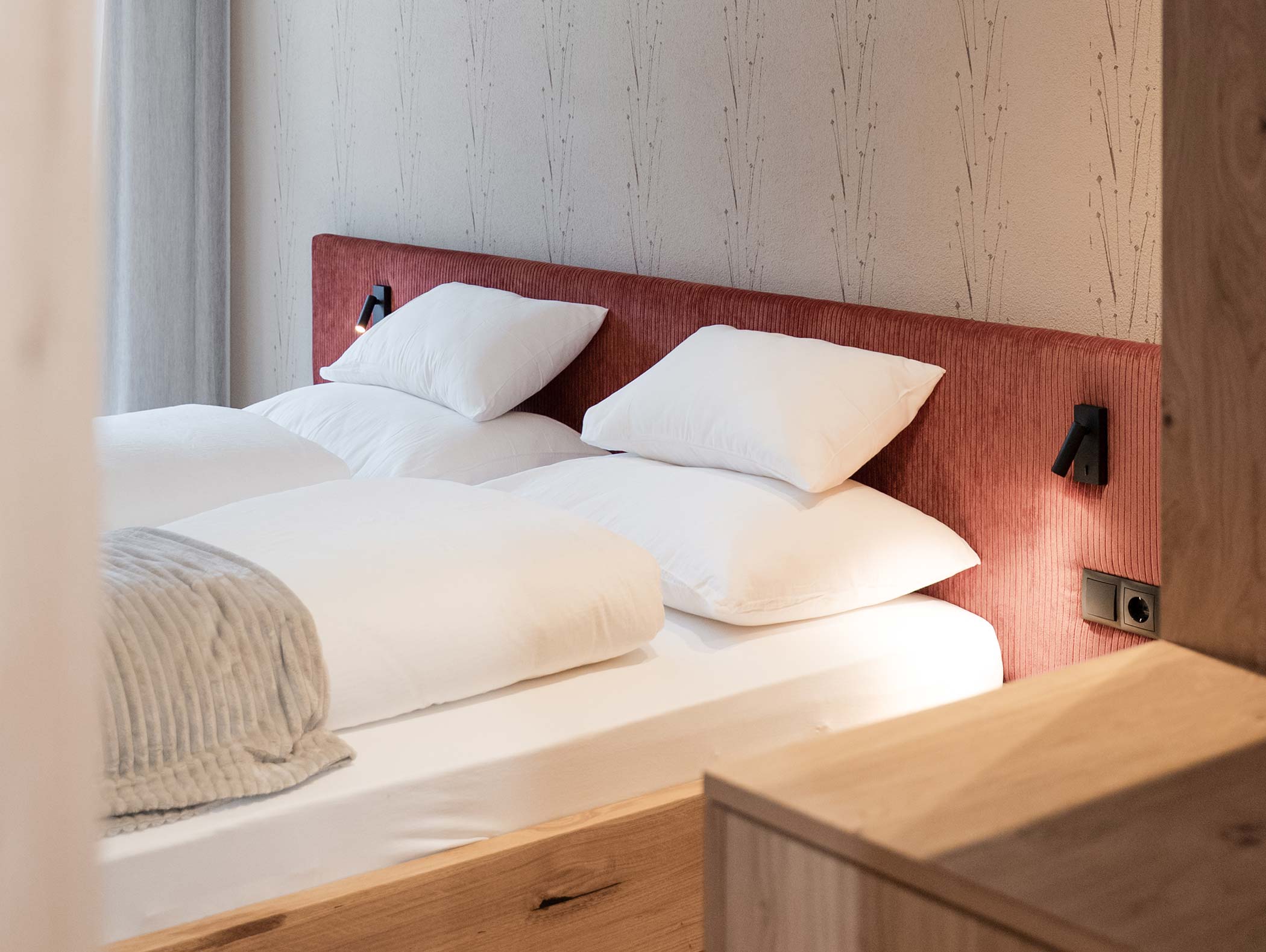 Modernes Schlafzimmer mit rotem Polsterkopfteil, weißem Bettzeug und an der Wand montierten Leselampen. - Hotel Moosmair