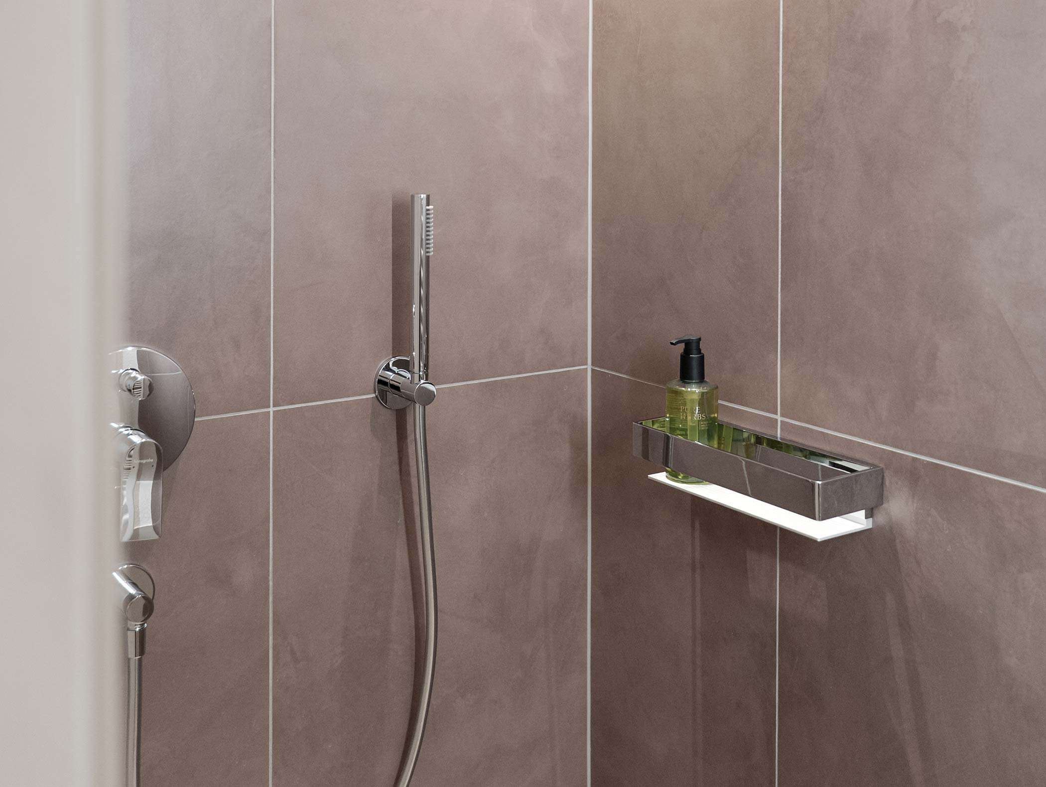 Moderne Dusche mit einer Handbrause und einer Ablage mit Seifenspender und einer kleinen Flasche. - Hotel Moosmair