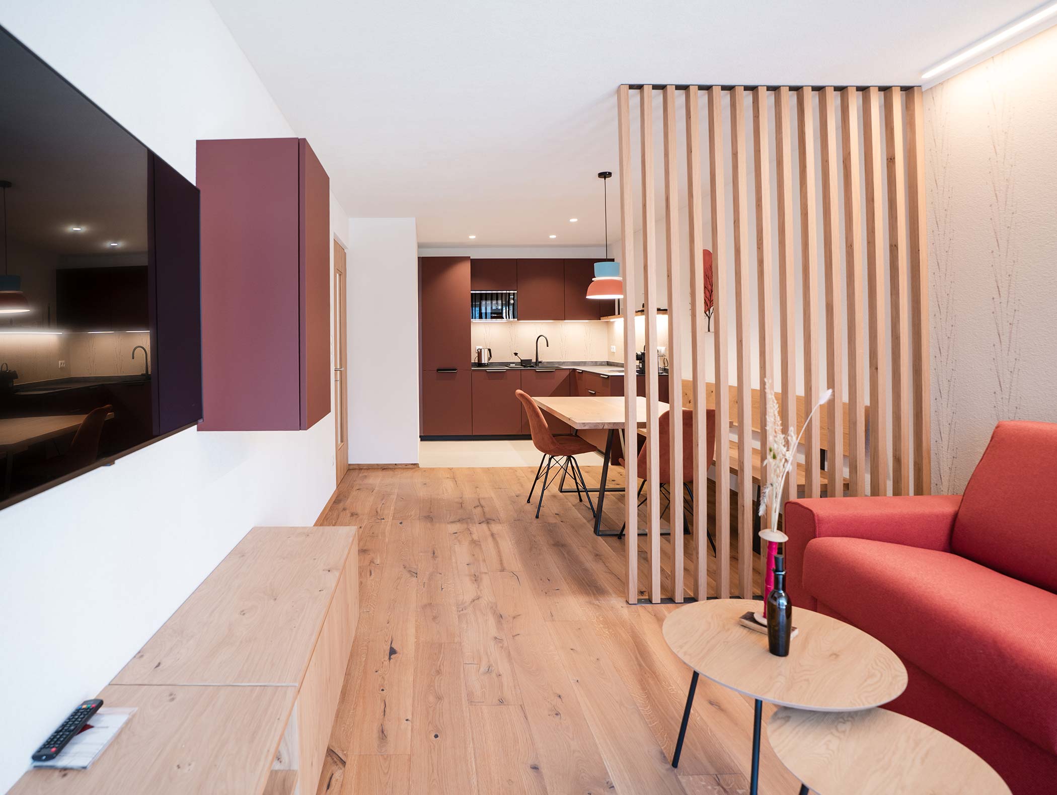 Modernes, offenes Wohnzimmer und Küche mit Holzfußboden, Trennwand aus Lattenrost und minimalistischen Möbeln. - Hotel Moosmair