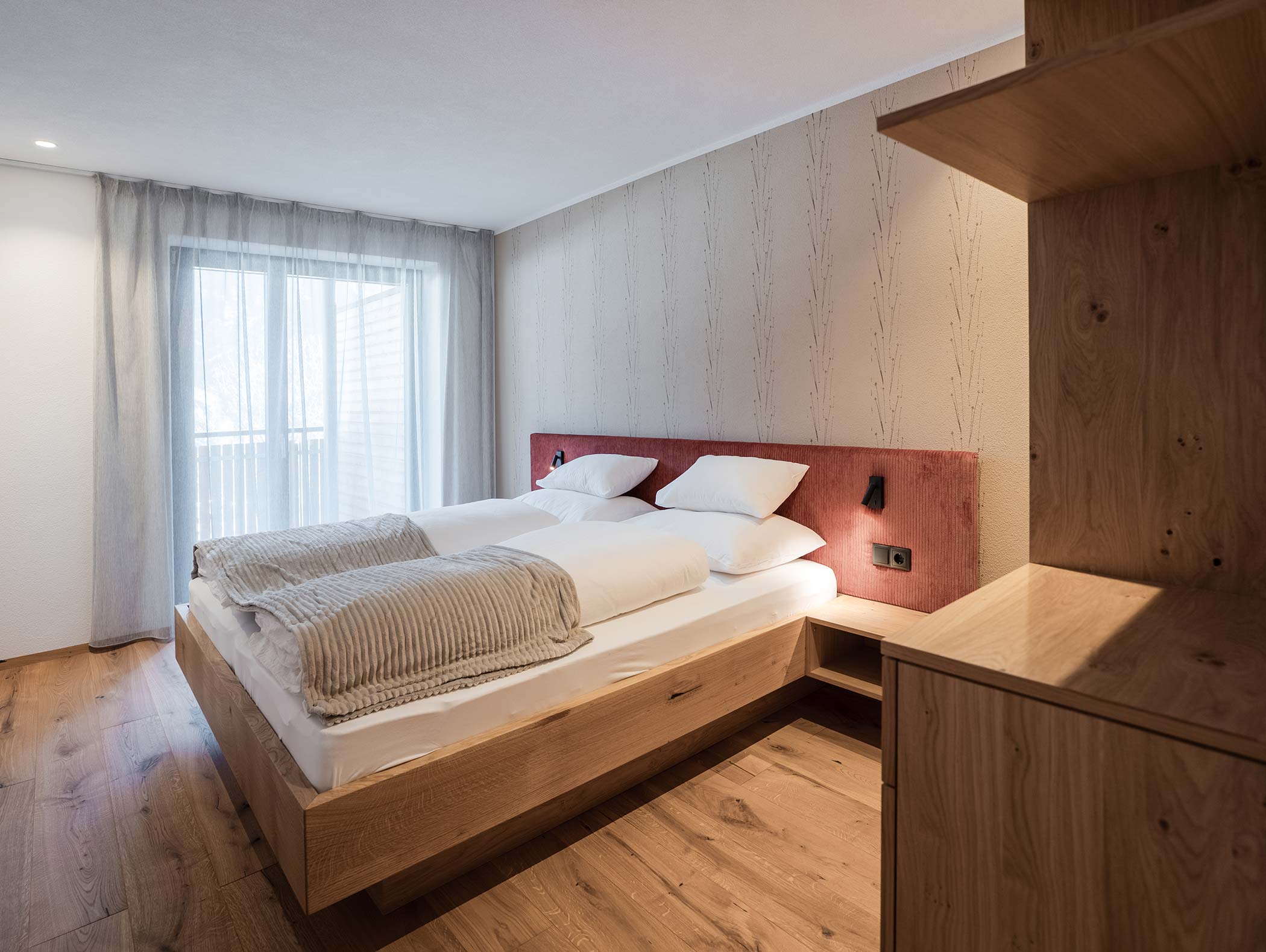 Modernes Schlafzimmer mit Holzbett, neutraler Bettwäsche, großem Fenster mit Gardinen und Holzboden. - Hotel Moosmair