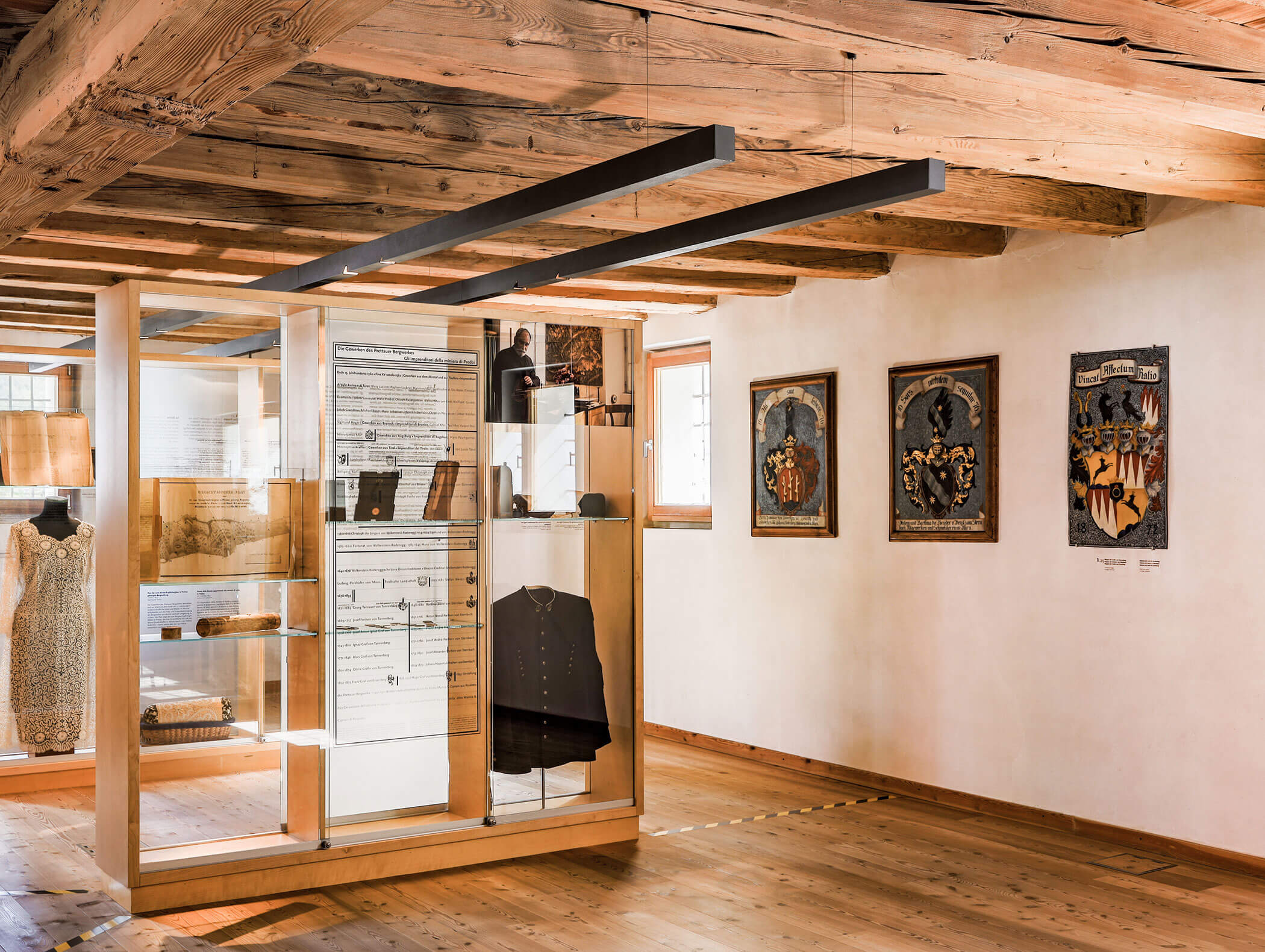 Hölzerner Museumsraum mit Vitrinen mit Kleidung und Artefakten und gerahmter historischer Kunst an den Wänden. - Hotel Moosmair