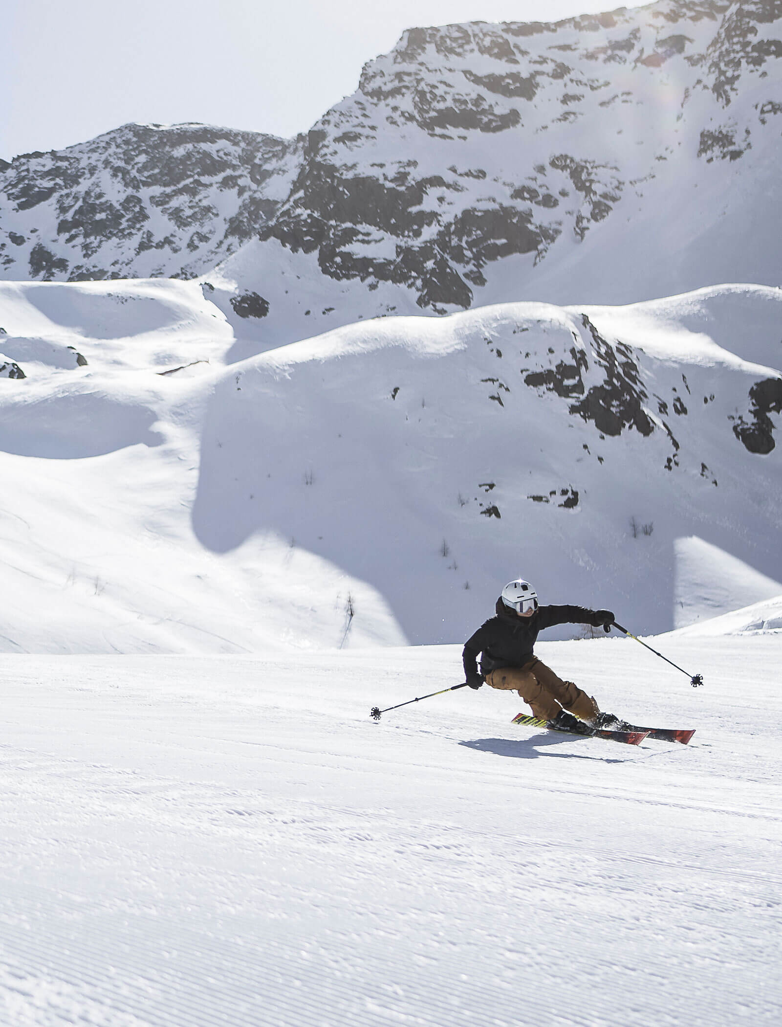 Skifahrer in Bewegung beim Abfahren eines verschneiten Berghangs mit schroffen Gipfeln im Hintergrund. - Hotel Moosmair