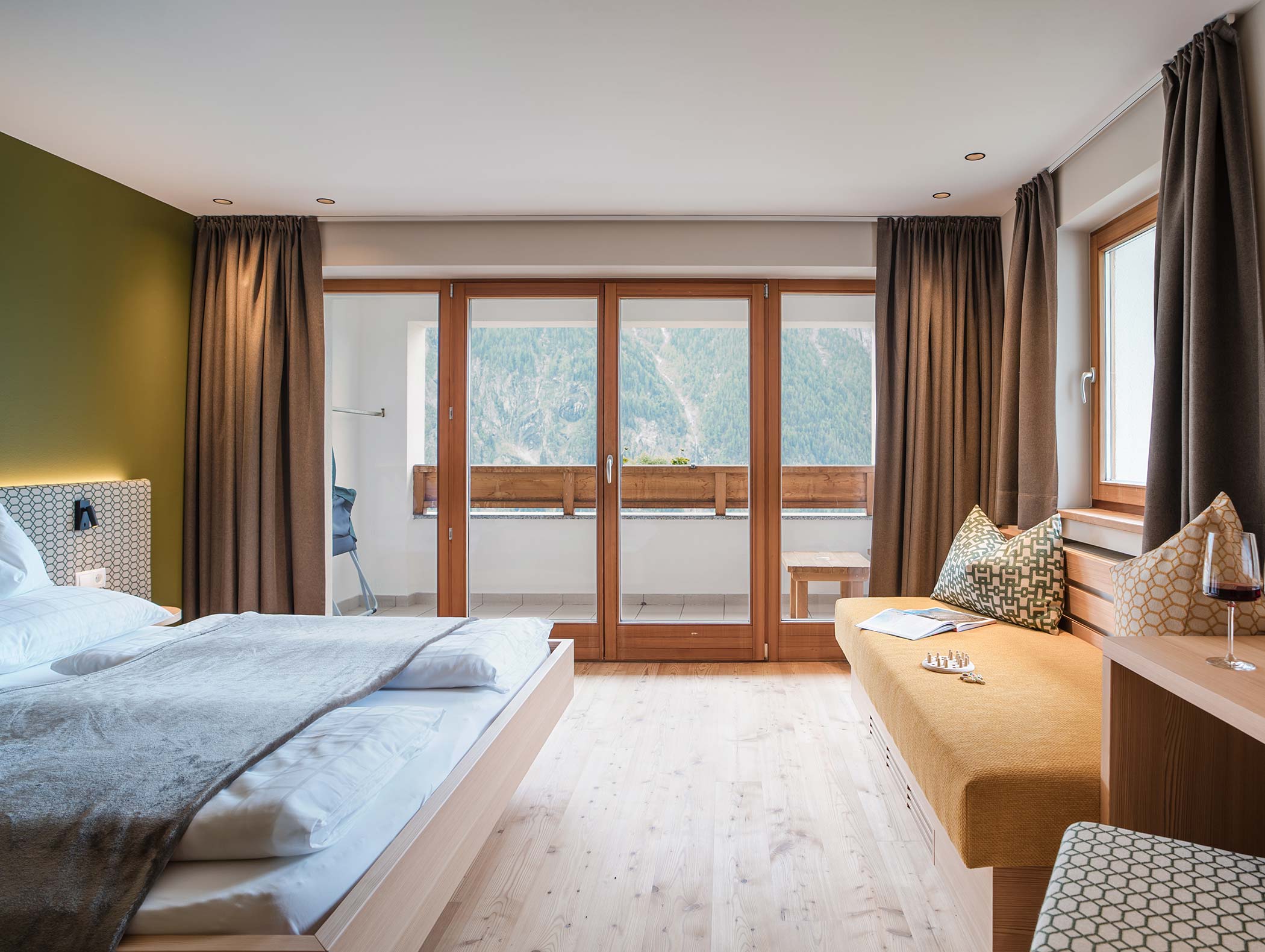 Modernes Hotelzimmer mit einem großen Bett, einer Sitzecke und einem Balkon mit Blick auf die Berge durch Glastüren. - Hotel Moosmair