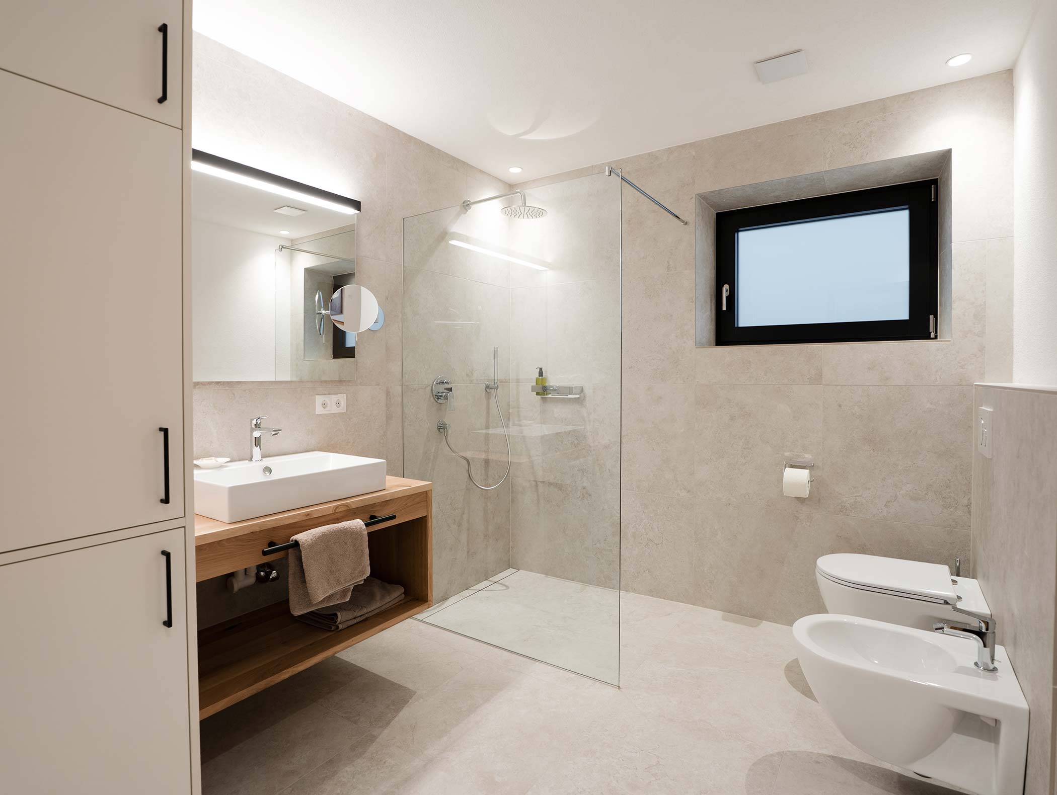 Modernes Badezimmer mit Glasdusche, Waschbecken, Bidet, Toilette und einem großen Spiegel in neutralen Farbtönen. - Hotel Moosmair