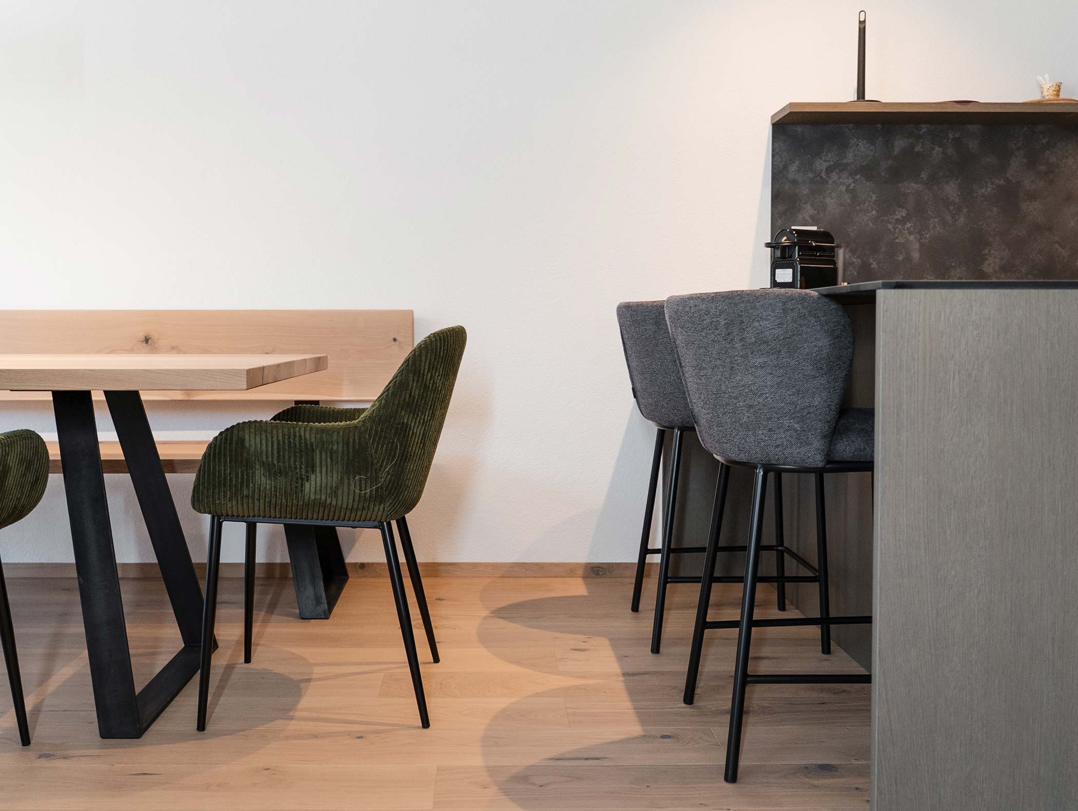 Moderner Essbereich mit Holztisch, grünem Stuhl und grauen Barhockern an einem Küchentresen. - Hotel Moosmair