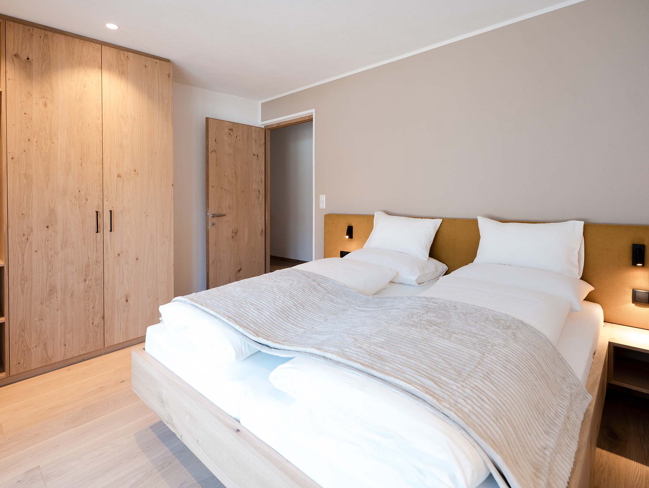 Minimalistisches Schlafzimmer mit einem Doppelbett, einem Holzschrank und einer offenen Tür in hellen, neutralen Tönen. - Hotel Moosmair