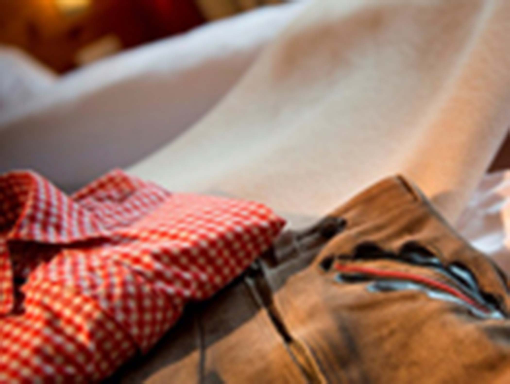 Rot kariertes Hemd und braune Hose mit Stickerei, auf einem Bett liegend, leicht unscharfes Bild. - Hotel Moosmair