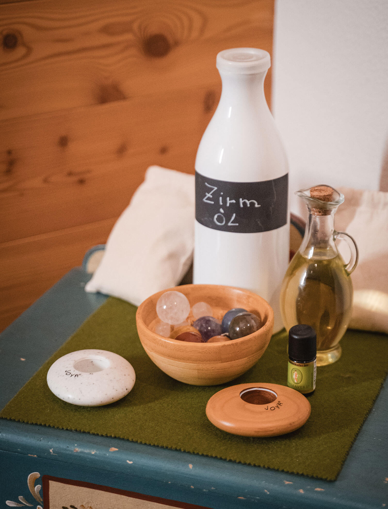 Eine Keramikflasche mit der Aufschrift Zirn Öl, ein Glasölkrug, Kristalle in einer Schale und Öle auf einer grünen Matte. - Hotel Moosmair